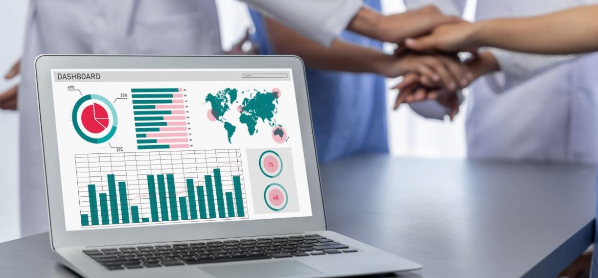 Computer with global graph images and ancillary supplies and equipment team placing hands over each other to show successful planning